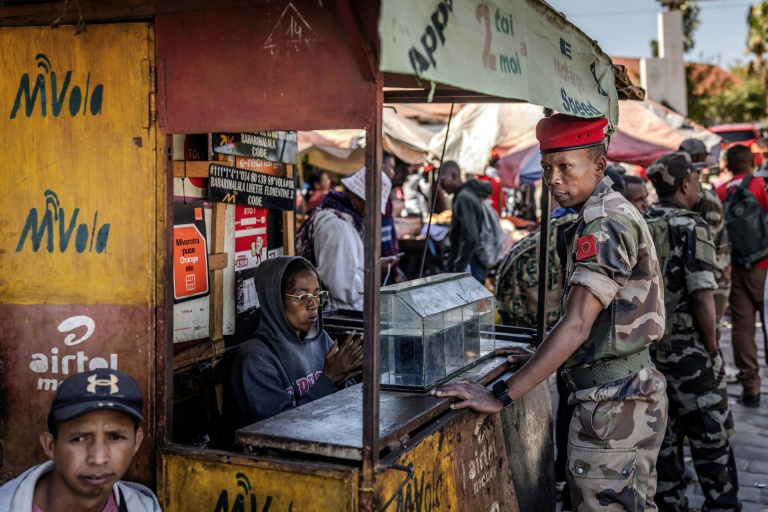 Au lendemain de la prise de pouvoir, un soldat de l'unité Capsat discute avec une vendeuse près de sa base militaire à Antananarivo, le 15 octobre 2025