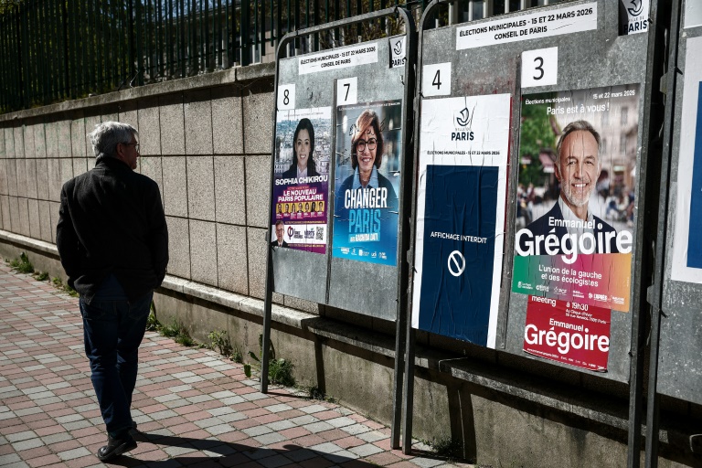 Une personne passe devant des affiches électorales pour les municipales, le 18 mars 2026 à Paris