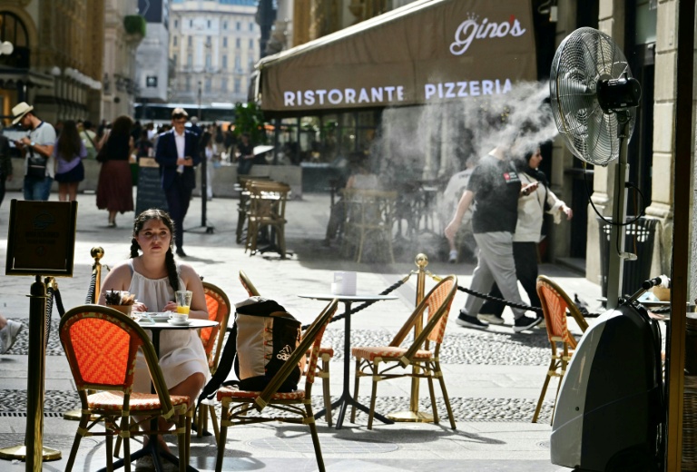 Une jeune fille assise à la terrasse d'un marchand de glaces, sur laquelle un ventilateur-brumisateur a été installé pour se protéger de la chaleur à Milan en Italie, le 27 mai 2026