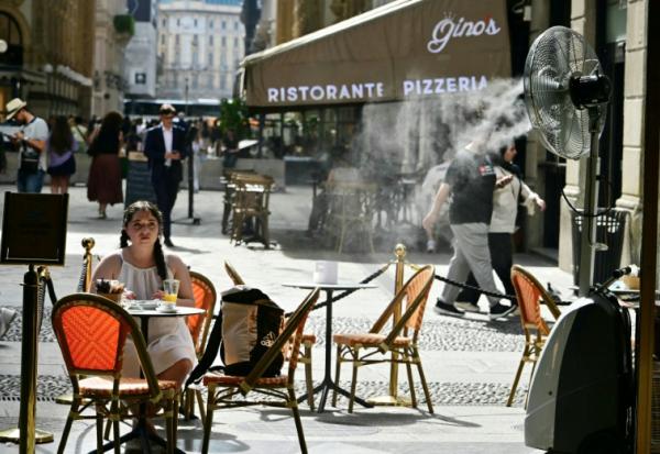 Une jeune fille assise à la terrasse d'un marchand de glaces, sur laquelle un ventilateur-brumisateur a été installé pour se protéger de la chaleur à Milan en Italie, le 27 mai 2026