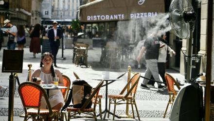 Une jeune fille assise à la terrasse d'un marchand de glaces, sur laquelle un ventilateur-brumisateur a été installé pour se protéger de la chaleur à Milan en Italie, le 27 mai 2026