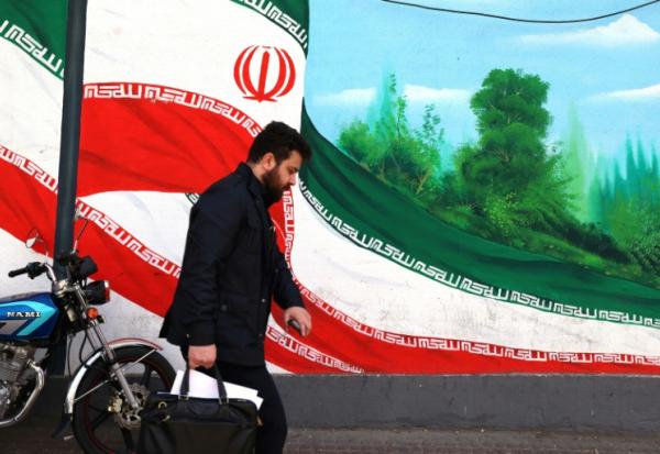 Une Iranien marche près d'une fresque représentant le drapeau national, à Téhéran le 22 février 2026