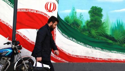 Une Iranien marche près d'une fresque représentant le drapeau national, à Téhéran le 22 février 2026