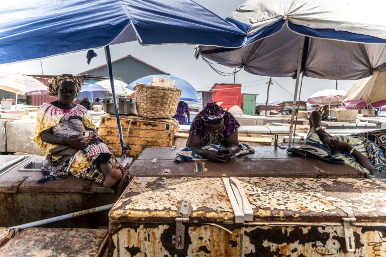 Des poissonniers se reposent sur leurs réfrigérateurs au point de débarquement des poissons à Tanji, en Gambie, le 12 septembre 2026, alors que les coupures d'électricité prolongées rendent difficile la conservation de leurs prises