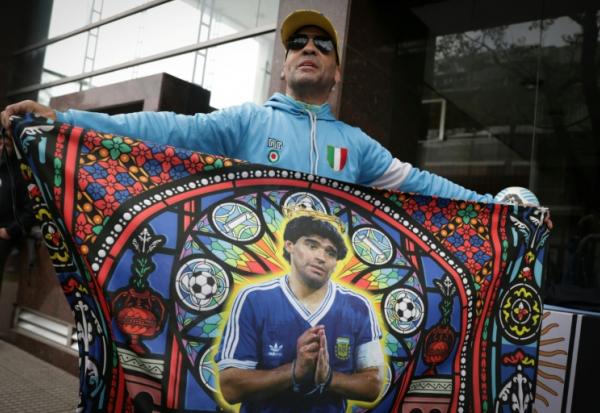 Un supporter tient un drapeau à l'effigie de Diego Maradona, avant une audience du procès sur le décès de la légende du football argentin, devant le tribunal à San Isidro, le 8 octobre 2026 en Argentine