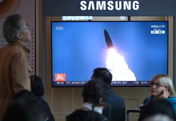 Des personnes sont assises devant un écran de télévision diffusant un journal télévisé avec des images d'archives d'un test de missile nord-coréen, dans une gare de Séoul, le 22 octobre 2025