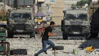 Un Palestinien court devant des véhicules militaires israéliens stationnés dans la vieille ville de Naplouse en Cisjordanie occupée, le 9 août 2022     
