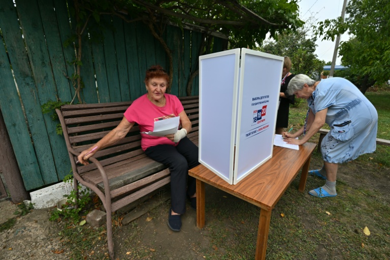 Une femme examine des bulletins de vote dans un bureau de vote mobile installé par les membres d'une commission électorale locale, accompagnés d'un militaire russe, à Novonikolayevka, dans la région de Donetsk, en Ukraine sous contrôle russe, le 14 septembre 2026