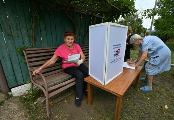 Une femme examine des bulletins de vote dans un bureau de vote mobile installé par les membres d'une commission électorale locale, accompagnés d'un militaire russe, à Novonikolayevka, dans la région de Donetsk, en Ukraine sous contrôle russe, le 14 septembre 2026