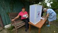 Une femme examine des bulletins de vote dans un bureau de vote mobile installé par les membres d'une commission électorale locale, accompagnés d'un militaire russe, à Novonikolayevka, dans la région de Donetsk, en Ukraine sous contrôle russe, le 14 septembre 2026