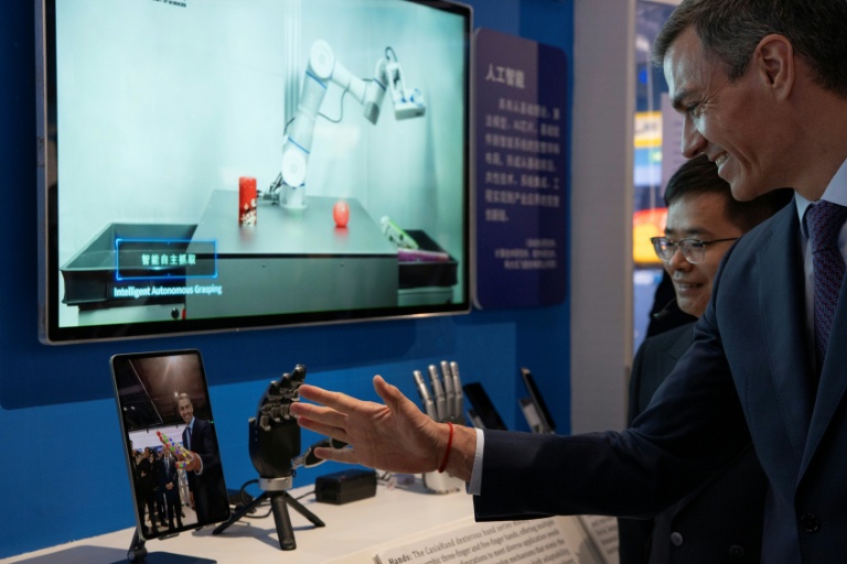 Le Premier ministre espagnol Pedro Sanchez observe une main robotisée lors d'une visite à l'Université de l'Académie chinoise des sciences à Pékin, le 13 avril 2026