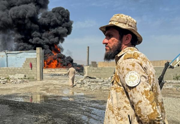 Un membre des forces de sécurité talibanes monte la garde alors que de la fumée s'élève du site de frappes aériennes pakistanaises sur des dépôts pétroliers, près de l'aéroport de Kandahar, le 13 mars 2026 en Afghanistan