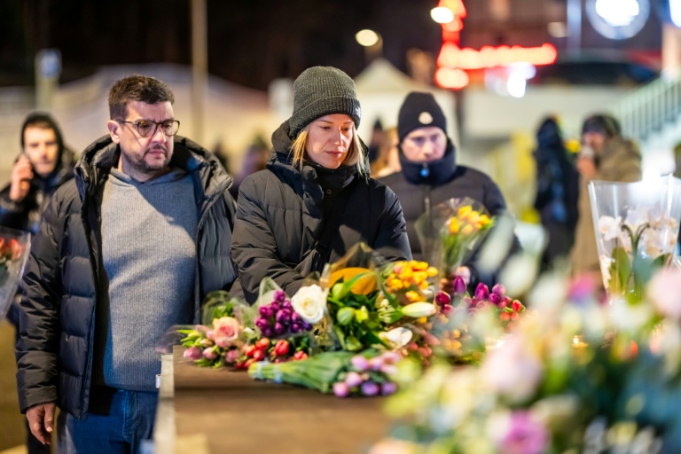 Des personnes en deuil se rassemblent devant des fleurs et des bougies déposées près du lieu où un incendie a ravagé un bar bondé lors des célébrations du nouvel an dans la station de ski alpine de Crans-Montana, le 1er janvier 2026 