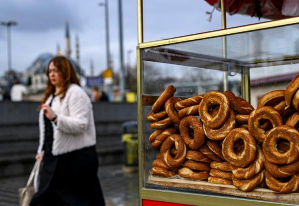 Une femme passe à côté d'un vendeur de simits, petits pains ronds turcs en forme d'anneau, le 27 décembre 2025 à Istanbul