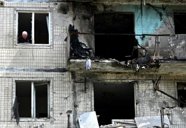 Un habitant à la fenêtre de son appartement dans un immeuble résidentiel endommagé par une frappe de drone russe sur Kiev, le 24 mai 2025 en Ukraine