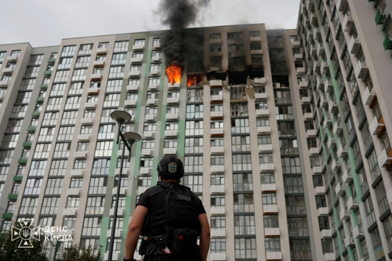 Photo prise et publiée par les services de secours ukrainiens le 1er septembre 2026, montrant un policier devant un immeuble d'habitation en feu à Kiev, après une frappe russe