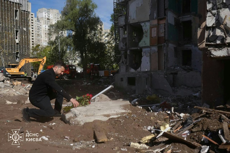 Photo prise et diffusée par les services d'urgence ukrainiens, le 15 mai 2026, montrant le président ukrainien Volodymyr Zelensky déposant des fleurs sur le site d'une attaque aérienne à Kiev
