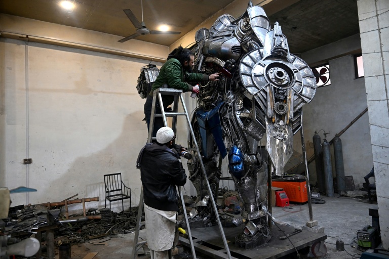 Le sculpteur Ehtisham Jadoon (en haut) peint à la bombe un Optimus Prime, personnage du film Transformers, fabriqué à partir de ferraille dans son atelier situé à la périphérie d'Islamabad, le 30 janvier 2026 au Pakistan