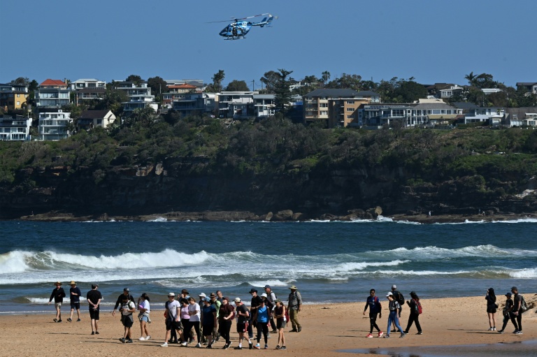 Des habitants marchent sur une plage de Sydney fermée à la suite d’une attaque de requin à Long Reef Beach tandis qu'un hélicoptère survole la zone, le 6 septembre 2025.