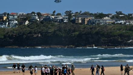 Des habitants marchent sur une plage de Sydney fermée à la suite d’une attaque de requin à Long Reef Beach tandis qu'un hélicoptère survole la zone, le 6 septembre 2025.