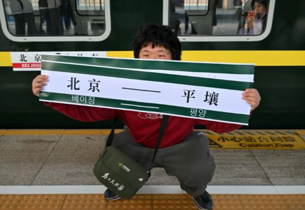 Un homme brandit une banderole "Pékin-Pyongyang" devant le train K27 à destination de Pyongyang, à la gare de Pékin, le 12 mars 2026 en Chine