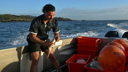 Charlie Kerr, membre du programme de surveillance des requins, prépare des lignes équipées d'hameçons appâtés reliées à des bouées connectées, le 10 novembre 2025 près de Coffs Harbour, en Nouvelle-Galles du Sud, en Australie